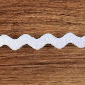 May include: White glitter zig zag trim. The trim is a wavy, zig zag shape and is made of white glitter fabric.