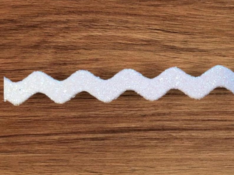 May include: White glitter zig zag trim. The trim is a wavy, zig zag shape and is made of white glitter fabric.