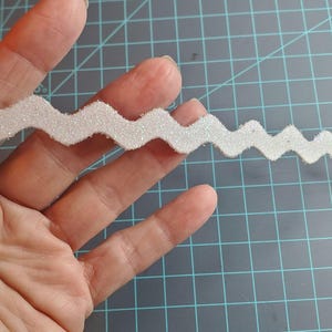 May include: White sparkly zig zag trim with a wavy edge.