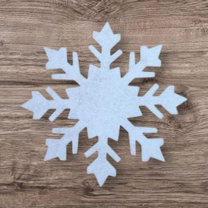 Peut inclure: Un flocon de neige en feutre bleu clair à six branches symétriques. Le flocon de neige est centré sur un fond en bois. Le design du flocon de neige présente des pointes et des découpes complexes.