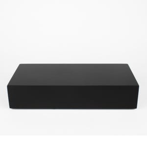 May include: A rectangular black box with a matte finish. The design is minimalist, with clean lines and a smooth surface. The object is set against a plain white background. The box appears to be made of wood.