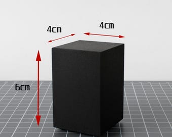 May include: A solid black rectangular block with a matte finish. Red arrows and text indicate the dimensions of the object, showing a width of 4cm, a depth of 4cm, and a height of 6cm. The object is positioned upright on a flat surface.
