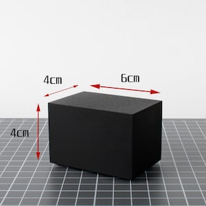 May include: A solid black rectangular block, 6 cm long, 4 cm wide, and 4 cm high. The block is displayed on a gray grid surface against a white background. The dimensions are clearly labeled in centimeters.