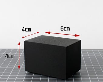May include: A solid black rectangular block, 6 cm long, 4 cm wide, and 4 cm high. The block is displayed on a gray grid surface against a white background. The dimensions are clearly labeled in centimeters.
