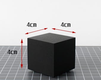 May include: A solid black cube, each side measuring 4cm. The cube is displayed on a grid surface, with arrows indicating the dimensions. The object is a simple geometric shape.