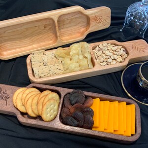 May include: Three wooden serving trays with different compartments for snacks. The trays are made of different types of wood and have a natural finish. The trays are filled with various snacks, including crackers, chips, nuts, dried fruit, and cheese.