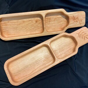 May include: Two wooden serving trays with a divided section and a carved leaf design. The trays are made of light wood and have a natural finish.