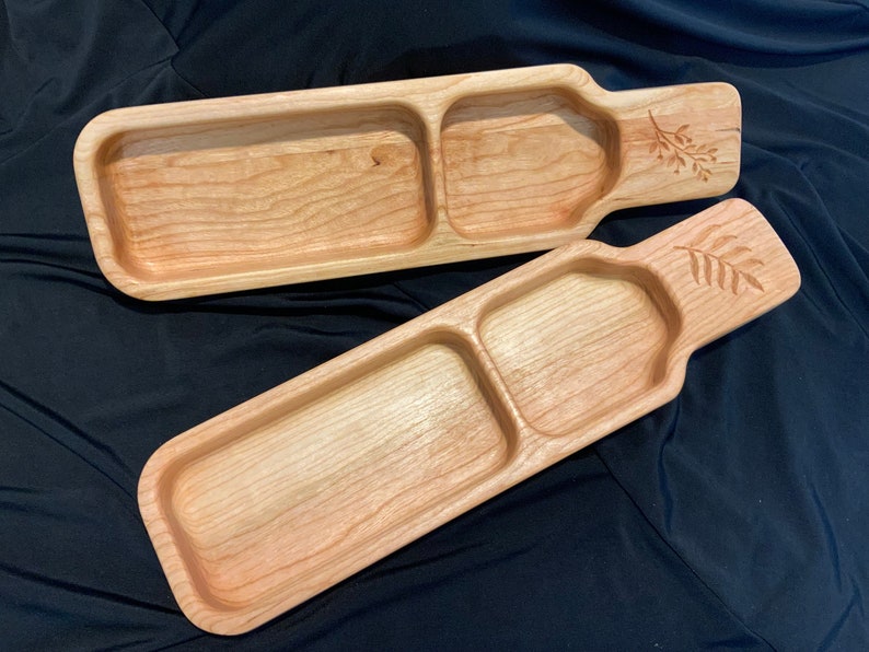 May include: Two wooden serving trays with a divided section and a carved leaf design. The trays are made of light wood and have a natural finish.