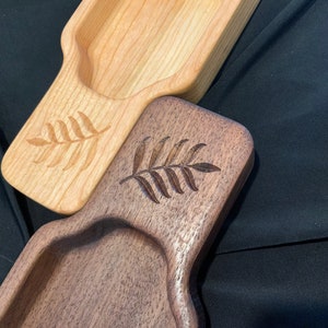 May include: Two wooden serving trays with a carved leaf design. The tray on top is light wood and the tray on the bottom is dark wood.
