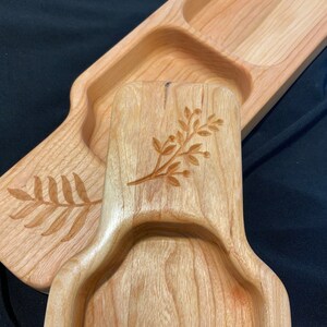 May include: A wooden serving tray with three separate compartments. The tray is made of light wood and has a natural finish. The compartments are decorated with engraved floral designs.