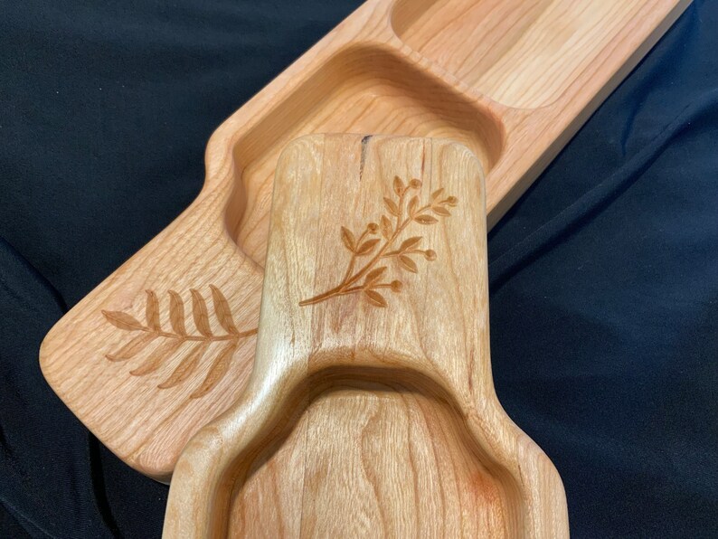 May include: A wooden serving tray with three separate compartments. The tray is made of light wood and has a natural finish. The compartments are decorated with engraved floral designs.