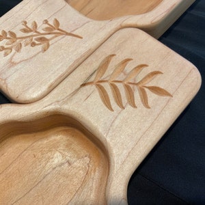 May include: Two wooden serving trays with carved leaf designs. The trays are made of light wood and have a natural finish.