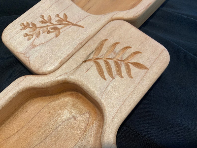 May include: Two wooden serving trays with carved leaf designs. The trays are made of light wood and have a natural finish.