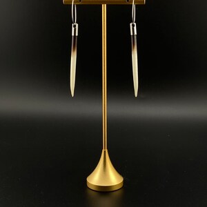 May include: A pair of long, white and brown earrings with silver hoops hanging from a gold stand.