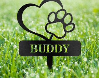 Op de afbeelding: Zwarte metalen tuinpaal met een hart- en pootafdrukontwerp. Het woord "BUDDY" is uitgesneden op een rechthoekig bord. De paal staat in groen gras.
