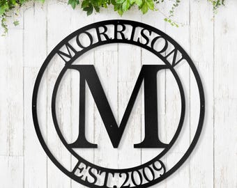 May include: Black metal circle sign with the last name "MORRISON" and the initial "M" in the center. The sign also includes the text "EST. 2009".