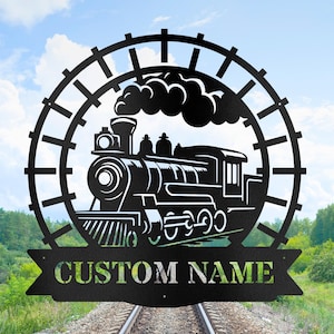 May include: Black metal train silhouette with the text "CUSTOM NAME" on a banner. The train is surrounded by a circular railroad track design. The background shows a blue sky with clouds and a green landscape.