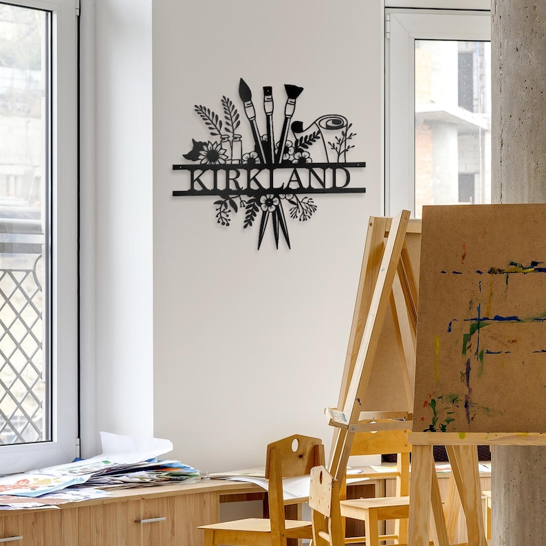 May include: Black metal wall art featuring a floral design with paintbrushes and a paint roller. The name "KIRKLAND" is displayed on a banner.