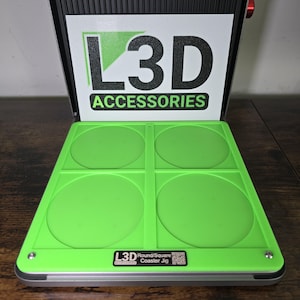 May include: A green and silver coaster jig with four circular molds. The jig is labeled "L3D Round/Square Coaster Jig".