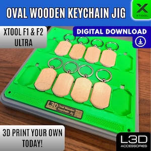 May include: A green jig holds multiple oval wooden keychains with silver rings. The text "OVAL WOODEN KEYCHAIN JIG" is at the top. The text "DIGITAL DOWNLOAD" and "3D PRINT YOUR OWN TODAY!" are also visible.