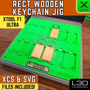 May include: A green rectangular keychain jig with wooden keychains and silver key rings. The jig has slots for the keychains and includes the text "RECT WOODEN KEYCHAIN JIG" and "XCS & SVG FILES INCLUDED!"