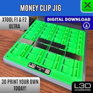 May include: A green money clip jig with silver and black clips. The text "MONEY CLIP JIG" is at the top. The text "XTOOL F1 & F2 ULTRA" is on the left. The text "DIGITAL DOWNLOAD" is on the right. The text "3D PRINT YOUR OWN TODAY!" is at the bottom.