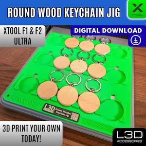 Peut inclure: Un gabarit vert avec des porte-clés ronds en bois et des anneaux argentés. Le gabarit est étiqueté "ROUND WOOD KEYCHAIN JIG" et "DIGITAL DOWNLOAD". Le texte "3D PRINT YOUR OWN TODAY!" est également visible.