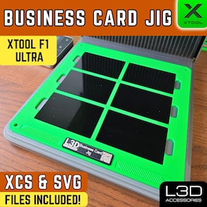 May include: A green and gray business card jig with black inlays. The text "BUSINESS CARD JIG" is at the top, with "XTOOL F1 ULTRA" below. The jig includes "XCS & SVG FILES INCLUDED!" and a logo that says "L3D ACCESSORIES".