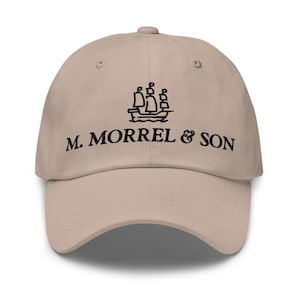 Op de afbeelding: Een beige baseballpet met een gebogen klep. De pet heeft zwarte tekst en een scheepsafbeelding. De tekst luidt "M. MORREL & SON". De pet heeft een ontwerp met zes panelen met een knoop aan de bovenkant.