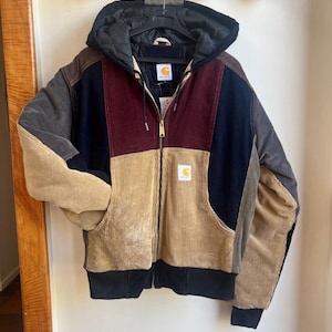 Puede incluir: Chaqueta de pana multicolor con capucha. La chaqueta presenta paneles de pana marrón, burdeos, azul marino y beige. Tiene una cremallera completa, dobladillo y puños de canalé negros y un pequeño parche con el logotipo.