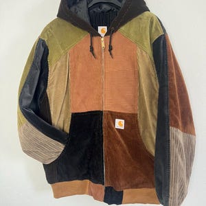 Könnte beinhalten: Eine Patchwork-Kapuzenjacke mit Reißverschluss aus Cordstoff in verschiedenen Erdtönen wie Braun, Olivgrün, Beige und Schwarz. Die Jacke verfügt über einen Frontreißverschluss, eine schwarze Kapuze und ein Carhartt-Markenlogo auf der Vordertasche.
