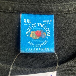 May include: Close-up of a black t-shirt with a blue tag. The tag reads "XXL ADULT" and "FRUIT OF THE LOOM 100% COTTON PRESHRUNK MADE IN U.S.A." The tag has a fruit graphic.
