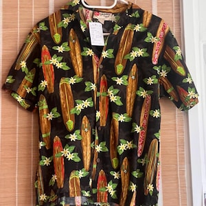 May include: A short-sleeved button-down shirt in black featuring a repeating pattern of brown surfboards and small white tropical flowers with green leaves. The shirt has a classic collar and a front button closure, displayed on a white hanger.