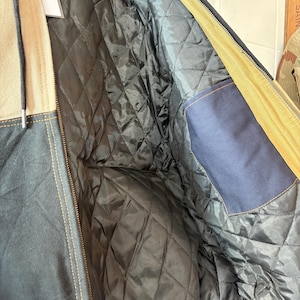 May include: A close-up of a navy blue and tan jacket with a quilted black lining. The jacket has a zipper closure and a blue pocket. The jacket's interior is visible, showcasing the diamond-patterned quilting.