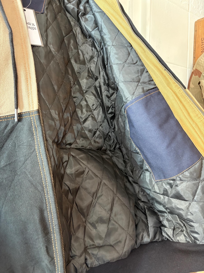 May include: A close-up of a navy blue and tan jacket with a quilted black lining. The jacket has a zipper closure and a blue pocket. The jacket's interior is visible, showcasing the diamond-patterned quilting.