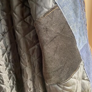 May include: Close-up of a blue denim jacket with a quilted black lining. The jacket features a dark gray herringbone pocket and a gold zipper. The interior lining is a diamond pattern.