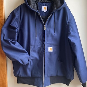 Peut inclure: Veste à capuche bleu marine avec doublure intérieure noire et fermeture éclair intégrale. La veste comporte une poche avant et un ourlet et des poignets côtelés noirs. Le logo Carhartt est visible sur la poche poitrine.