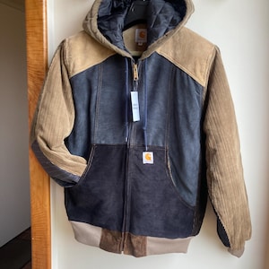 May include: A multi-toned Carhartt jacket with a hood. The jacket features a mix of corduroy and quilted materials in shades of brown, tan, and navy blue. It has a full zipper closure and a Carhartt logo patch on the front pocket.