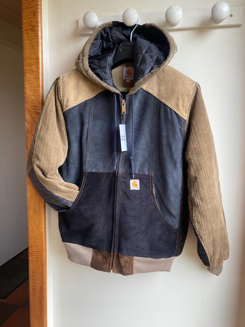 May include: A multi-toned Carhartt jacket with a hood. The jacket features a mix of corduroy and quilted materials in shades of brown, tan, and navy blue. It has a full zipper closure and a Carhartt logo patch on the front pocket.