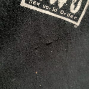 May include: Close-up of a black t-shirt with the white text "nWo new world order" in a rectangular box. The fabric shows slight wear and tear.