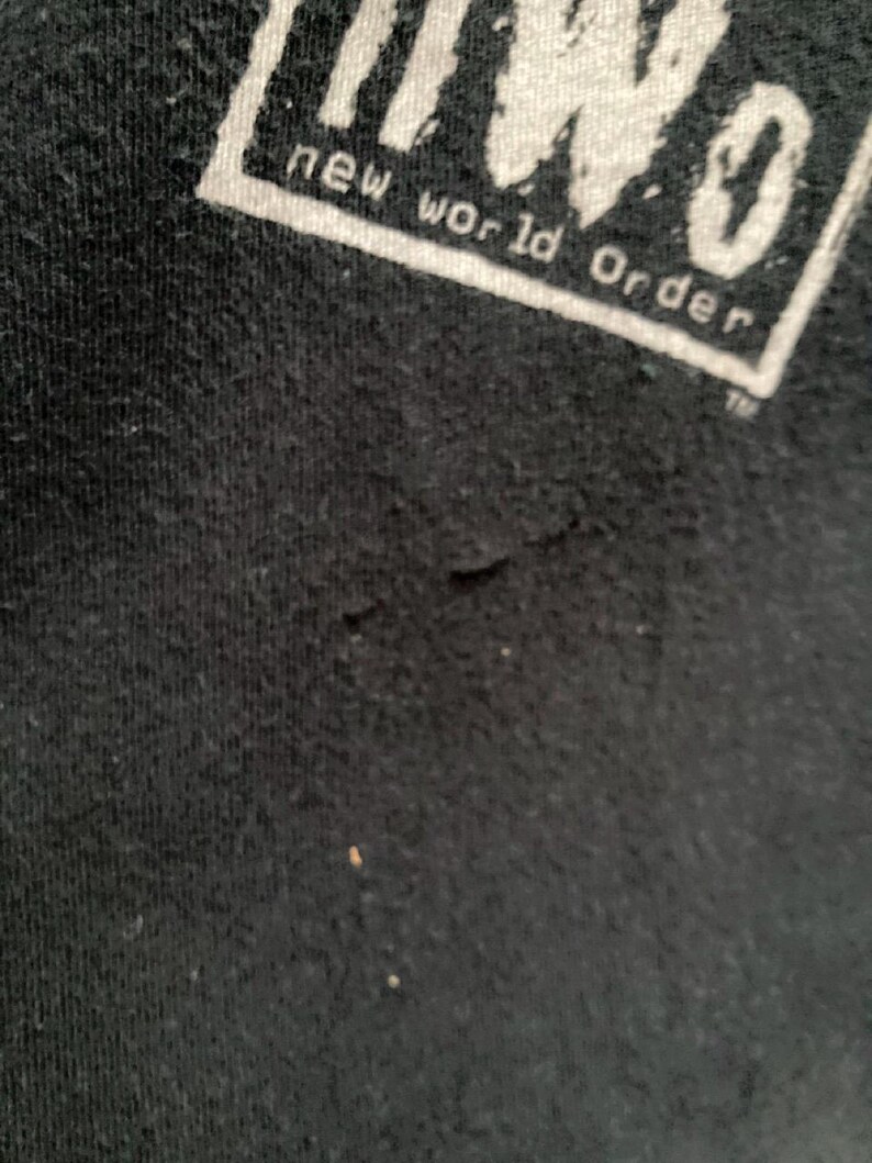 May include: Close-up of a black t-shirt with the white text "nWo new world order" in a rectangular box. The fabric shows slight wear and tear.