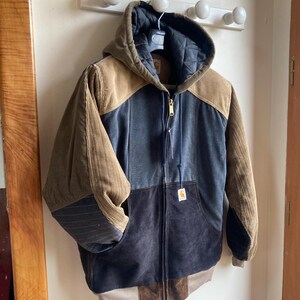 May include: A multi-toned corduroy jacket with a hood, hanging on a white wall. The jacket features panels of brown, blue, and black corduroy. It has a full zipper closure and a small logo tag. The jacket is approximately 28 inches long.