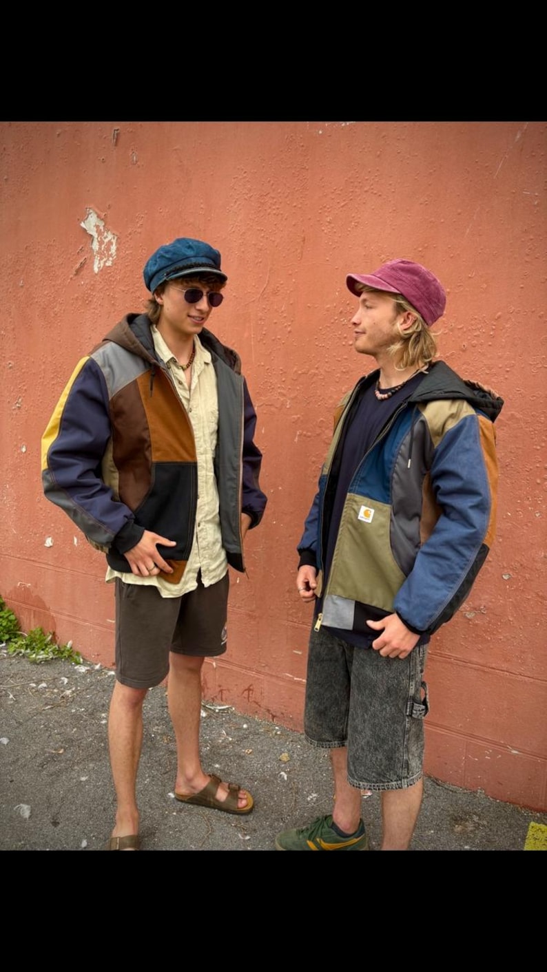 May include: Two people wearing patchwork jackets with a variety of colors including blue, brown, yellow, and gray. One person wears a blue cap and sunglasses, the other a maroon cap. Both wear shorts and sneakers or sandals. The jackets have a hooded design.