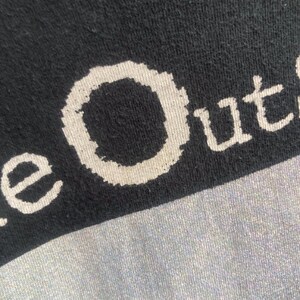 May include: Close-up of a black t-shirt with the white text "e Out". The fabric has a slightly textured appearance. The shirt is likely made of cotton or a similar material.