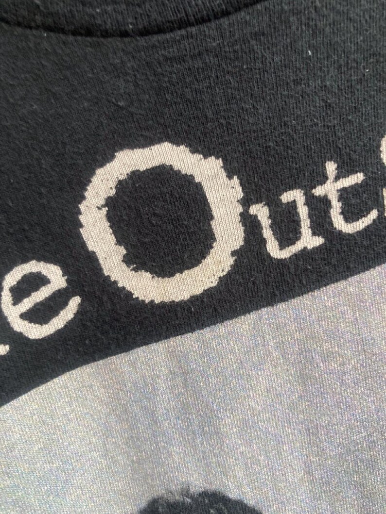 May include: Close-up of a black t-shirt with the white text "e Out". The fabric has a slightly textured appearance. The shirt is likely made of cotton or a similar material.