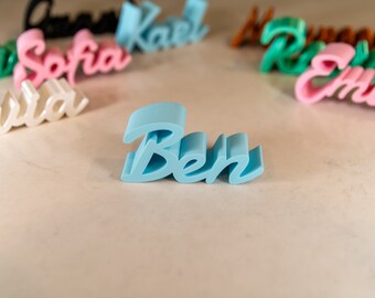 Könnte beinhalten: Ein hellblaues, 3D-gedrucktes Namensschild mit der Aufschrift "Ben".