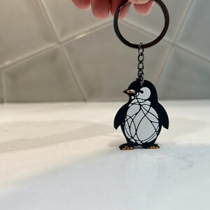 May include: A black and white penguin keyring with a black chain and a silver ring. The penguin has a white body with black wings and a black beak.
