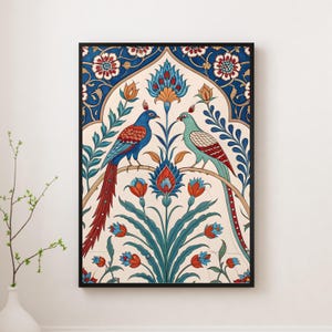 Puede incluir: Impresión artística enmarcada que presenta dos aves estilizadas posadas en una rama, rodeadas de diseños florales y foliares. La obra de arte muestra una vibrante paleta de colores azul, rojo, verde y crema, sobre un fondo crema, todo dentro de un marco negro.