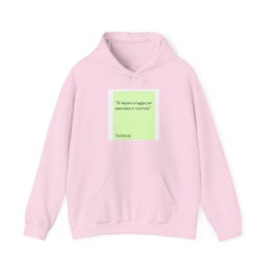 Può includere: Una felpa con cappuccio rosa chiaro caratterizzata da una grafica quadrata centrale. La grafica è un rettangolo verde chiaro contenente il testo "Si impara la legge per esercitare il controllo" seguito dal nome "Ted Bundy" in nero.