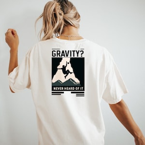 May include: White t-shirt with a black graphic of a rock climber on a cliff. The graphic says "GRAVITY? NEVER HEARD OF IT."